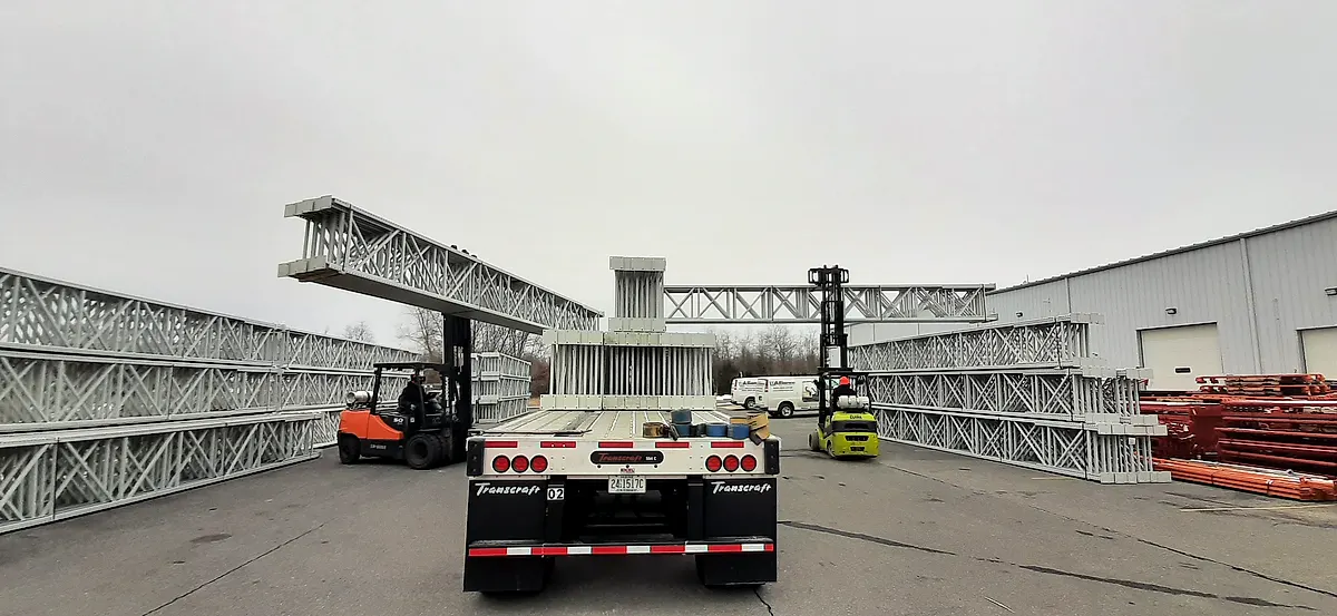 Flatbed truck of pallet rack frames being unloaded by forklift