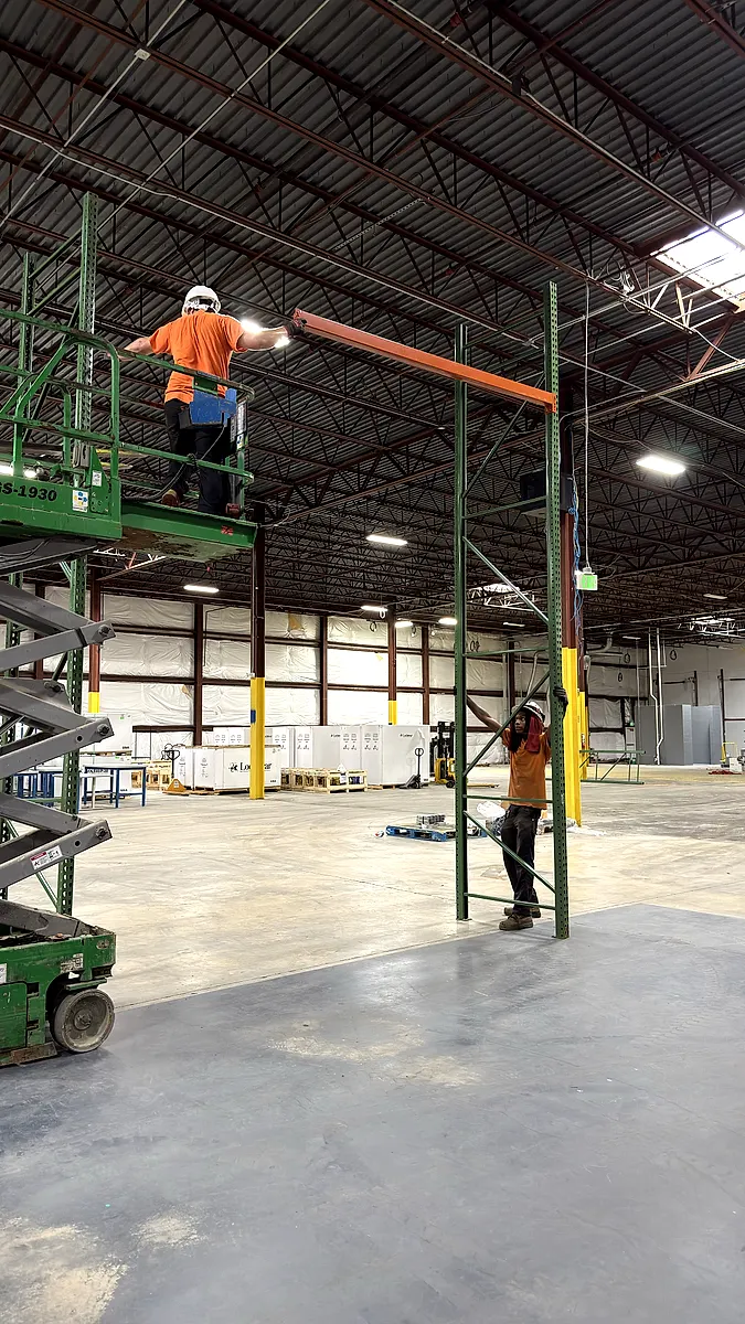 Installer on a scissor lift setting an upper pallet rack beam